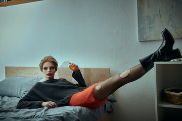A woman in a stylish grunge outfit poses on a bed with legs extended.