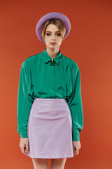 A woman in a lavender mini-skirt and green shirt poses against an orange background.