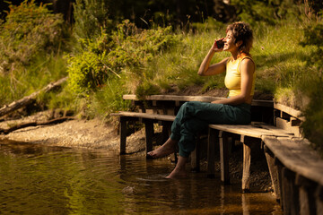 A woman is sitting on a bench by a body of water, talking on her cell phone