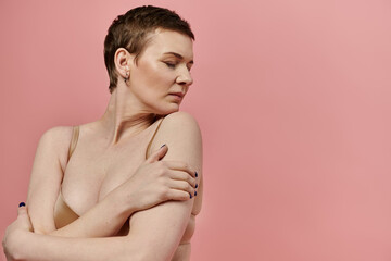 Short-haired woman with arms crossed against pink background; powerful display for breast cancer awareness