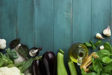 Rustic wooden food background empty frame border. Culinary border of bunch of basil, cauliflower, zucchini, garlic, olive oil in bottle and old pepper mill on rustic blue wood kitchen table. Top view