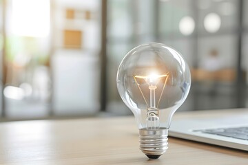 Close-up of a glowing light bulb on a wooden desk in a modern office environment.