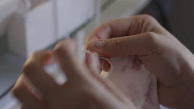 Woman tying threads after sewing up the edge of the fabric on an overlock sewing machine, close-up