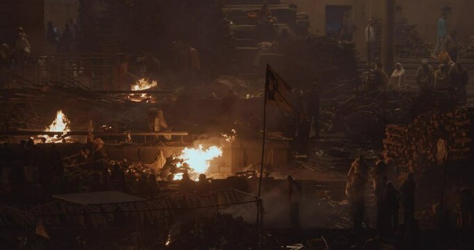 Varanasi, Uttar Pradesh, India. Cremation in process on Manikarnika Ghat. Cinematic Camera movement moving along riverbank embankment. View from riverside. night lights. Fire, smoke - Funeral rites of