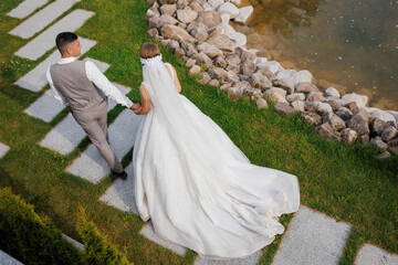 A bride and groom are walking down a stone path. The bride is wearing a white dress and a veil