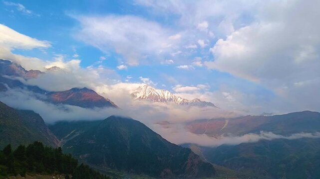 Timelapse of Himalayan mountain and drifting clouds with colourful rainbow in blue sky. The video taken in dusk before sunset. The mountain peak in uttarakhand covered in snow.