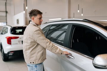 Thoughtful male visitor walking in modern auto showroom and choosing new vehicle to buy or rent....