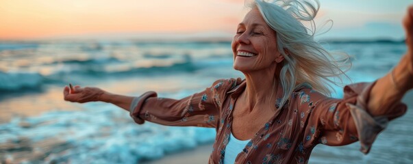 A senior woman is standing on the beach, smiling and waving her arms.