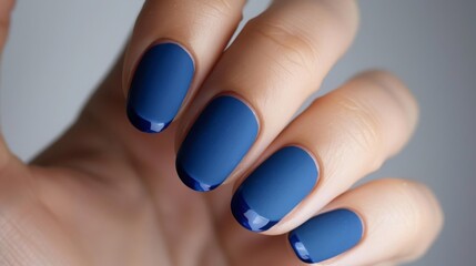 A close-up of a hand with matte blue nail polish and a dark blue tip on each nail.