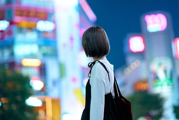 夜の繁華街を見つめる若い女性