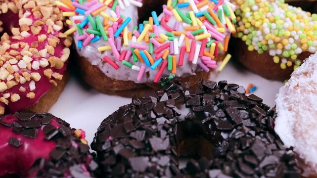 Donuts with different red, pink, chocolate icing lie in a white box, close-up top view