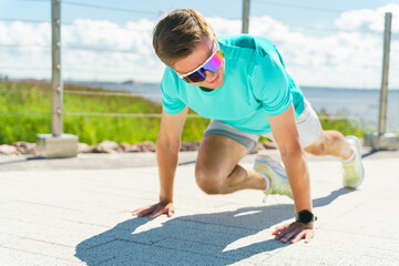 A man performing mountain climbers outdoors, focused on his workout under a bright blue sky by the waterfront.