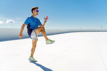 Smiling athlete in blue performing a high knee exercise under a clear sky, exuding energy and...