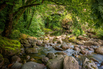 Argonza River as it passes through the medieval town of B&aacute;rcena Mayor, Cantabria, Spain, with rocks in its bed and a bridge in the background