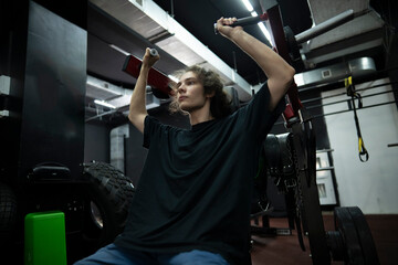 man in a black t-shirt performs a shoulder press exercise at a gym, lifting weights with his arms...