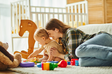 A young mother joyfully interacts with her toddler daughter on the floor at home, creating precious memories together.