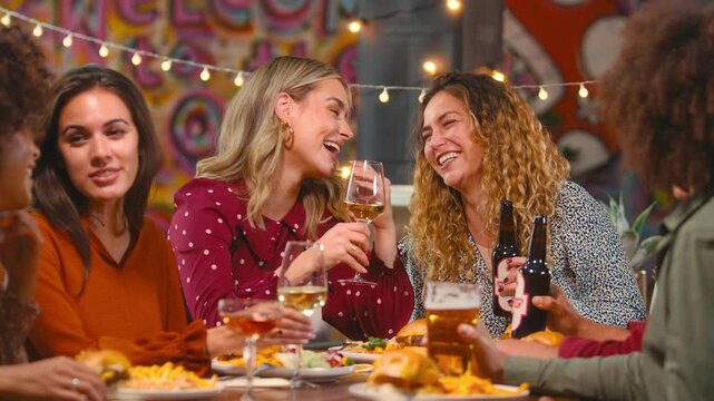 Group of multi-cultural friends sitting at table in restaurant eating meal and drinking on night out together- shot in slow motion