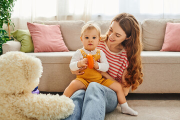 A young mother sitting on the floor, holding her baby daughter close in a loving embrace at home.