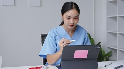 Female healthcare professional in scrubs using a tablet in a modern office, focused on work and note taking in a medical setting - Powered by Adobe