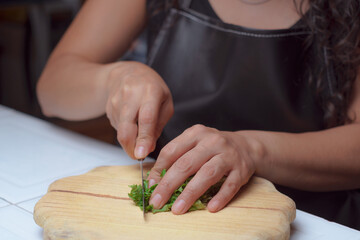 Hands of a cook with a knife cutting fresh lettuce leaves.