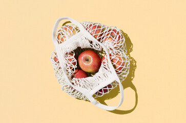 Red apples in a reusable mesh bag on a beige background. Zero waste concept