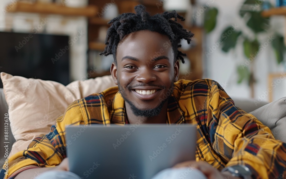 Poster a man with dreadlocks is smiling and holding a laptop. he is sitting on a couch and he is enjoying h