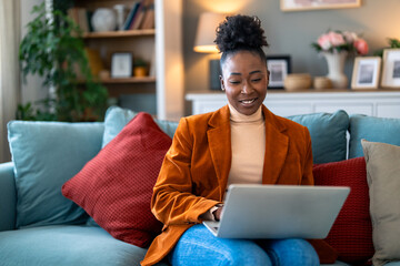 Content young businesswoman typing on a laptop, writing an e-mail, working and smiling. Home office...