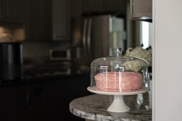 Strawberry pink homemade cake on the marble counter in glass dome with a dark background, space for copy on left, horizontal