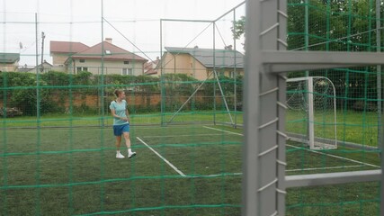 A female football coach and a male football player are training on a small football field. The woman takes a free kick, and the guy saves it. The shot is framed through the field's net. - Powered by Adobe