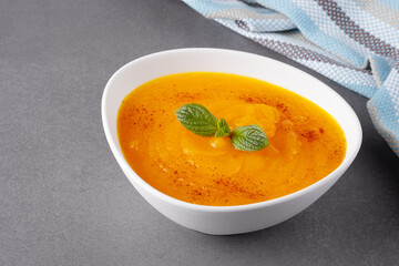 White bowl of pumpkin soup on a gray table