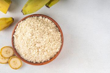 Alternative organic banana flour with fresh whole and sliced green bananas on white table background