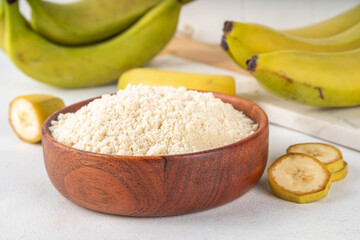 Alternative organic banana flour with fresh whole and sliced green bananas on white table background