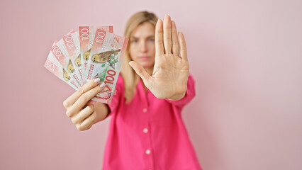 A young blonde woman in a pink shirt extends her hand to refuse new zealand currency against a...