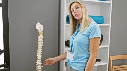 Blonde woman healthcare professional presenting spine model in clinic interior.