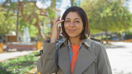 Smiling middle-aged hispanic woman adjusting glasses in a sunny park setting, exuding confidence and casual style