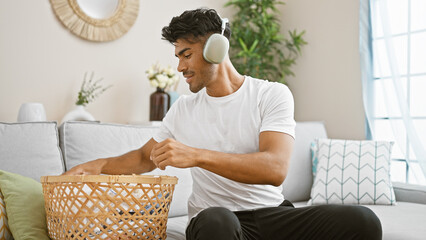 Handsome hispanic man listening to music on headphones while doing laundry at home
