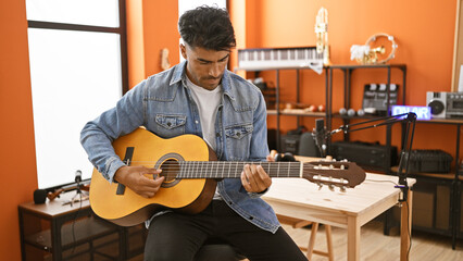 Handsome hispanic man playing guitar in a music studio with recording equipment