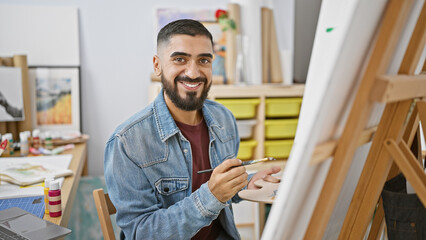 Handsome young man with beard painting on easel in bright art studio