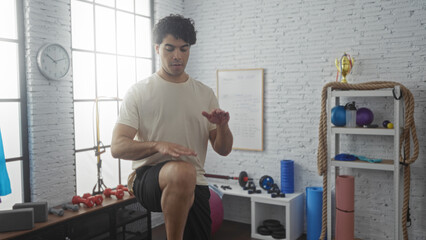 Young hispanic man exercising indoors in a gym surrounded by fitness equipment, demonstrating...