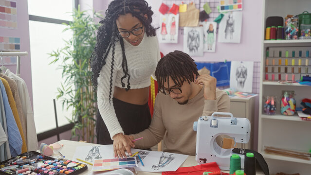 A woman and a man collaborate in a vibrant tailor shop examining fabric swatches and design sketches.