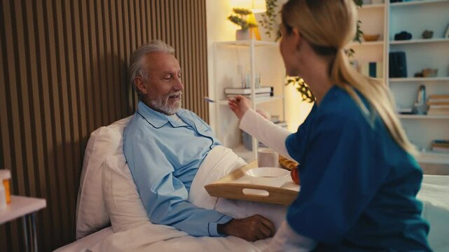 Nurse feeding senior bedridden male patient with a spoon, home care services