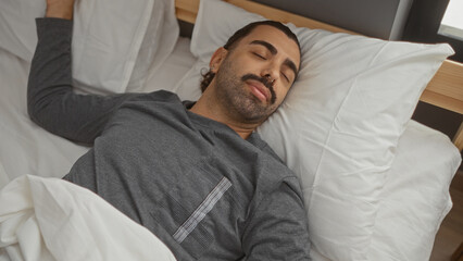 Fototapeta premium Handsome man with moustache sleeping peacefully on a bed in a cozy bedroom with white pillows and wooden headboard