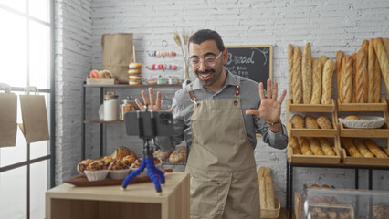 Young man with moustache filming video with smartphone in bakery shop surrounded by bread and pastries in an indoor setting