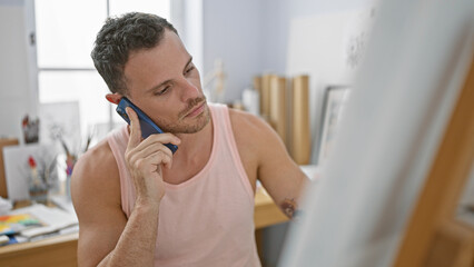 A handsome young man talking on a phone in his indoor home office, conveying focus and professionalism.