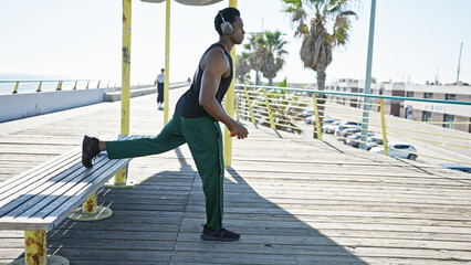 An athletic african american man stretching on a sunny urban boardwalk by the sea