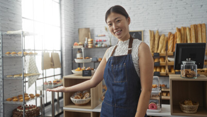 Asian woman wearing an apron smiling and gesturing towards a variety of baked goods inside a stylish, modern bakery shop in china.