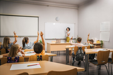 Young students raise his hands to answer a question during a lesson
