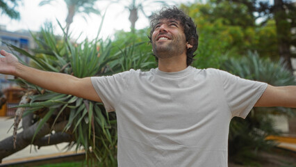 Young man enjoying a vibrant day outdoors in an urban park with arms wide open and a joyful expression