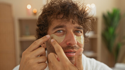 Handsome man applying eye patches in a spa wellness center indoors for beauty and relaxation.