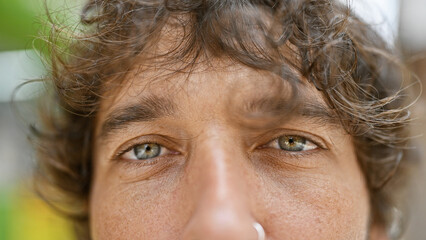 Close-up portrait of a handsome hispanic man with curly hair outdoors in a city environment.